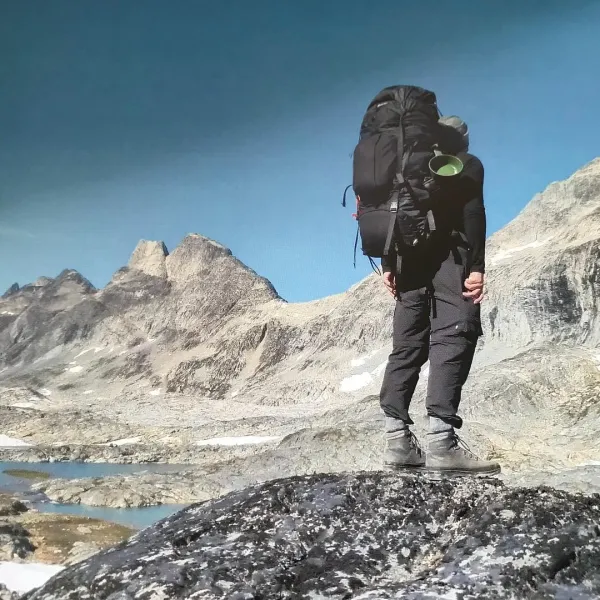 Wandelaar met grote rugzak op een rots tussen de bergen in Groenland